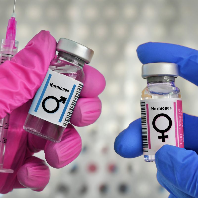 Transgender hormone therapy injections concept - vials of testosterone male and estrogen female horm